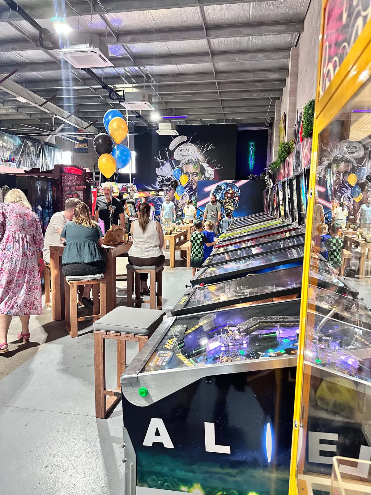 Families at the party tables in Castlecade with arcade machines and murals